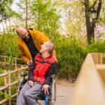 persona-discapacidad-silla-ruedas-empujada-amigo-parque-publico-ciudad-mirando-paisaje_242111-21542